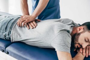 A chiropractor gently adjusting a person's back in a bright, calm clinical setting.