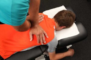 A chiropractor gently adjusts a patient's back in a calm, well-lit clinic room.