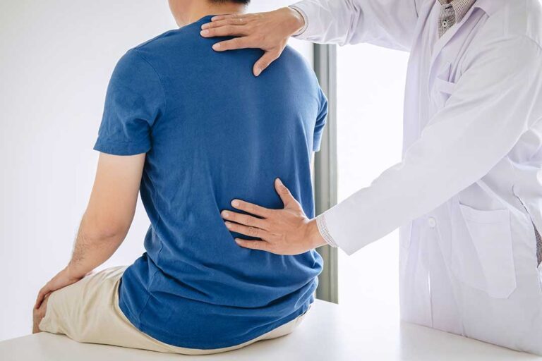 Person gently rotating a shoulder while seated, with one hand supporting the upper arm.